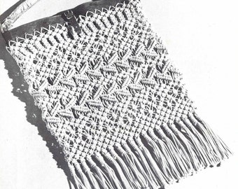 Puede incluir: Un bolso de macramé blanco con una correa de cuero y flecos. El bolso está hecho con una técnica de anudado y tiene un patrón geométrico.