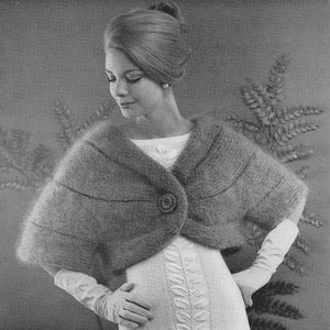 May include: A gray knitted shrug with a single button closure. The shrug is worn over a white dress with a lace pattern.