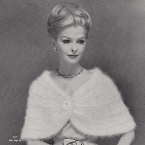 Puede incluir: Una mujer lleva una estola de punto blanco con un botón de imitación de perla. Lleva el pelo recogido en un moño alto y un collar de perlas.