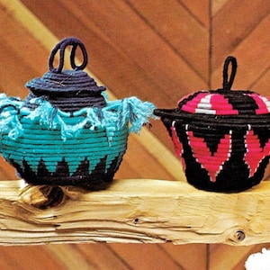 May include: Two woven baskets with lids, one is black with turquoise and blue accents, the other is black with pink and white accents.