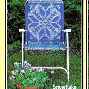 May include: A blue and white patterned metal folding chair with a silver frame. The chair is sitting on a green lawn with a potted plant in front of it. The plant has purple and white flowers. The text "Snowflake page 8" is printed below the chair.
