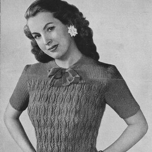 Könnte beinhalten: Ein Schwarzweißfoto einer Frau, die einen Strickpullover mit einem Blattmuster trägt. Der Pullover hat kurze Ärmel und eine Schleife am Ausschnitt. Der Text "IN LEAF PATTERN AND RIBBING LONG OR SHORT SLEEVES MEDIUM SIZE (2-ply)" ist oben im Bild gedruckt.