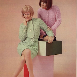 Puede incluir: Dos mujeres con suéteres de punto. La mujer de la izquierda lleva un suéter verde claro con cuello blanco y un botón dorado. La mujer de la derecha lleva un suéter rosa. Están sentadas en una plataforma multicolor.