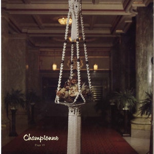 Peut inclure: Un porte-plante en macram&eacute; blanc avec un pompon, suspendu au plafond dans une pi&egrave;ce avec un tapis rouge. Le porte-plante est rempli de fleurs s&eacute;ch&eacute;es et comporte des perles noires sur les cordons.