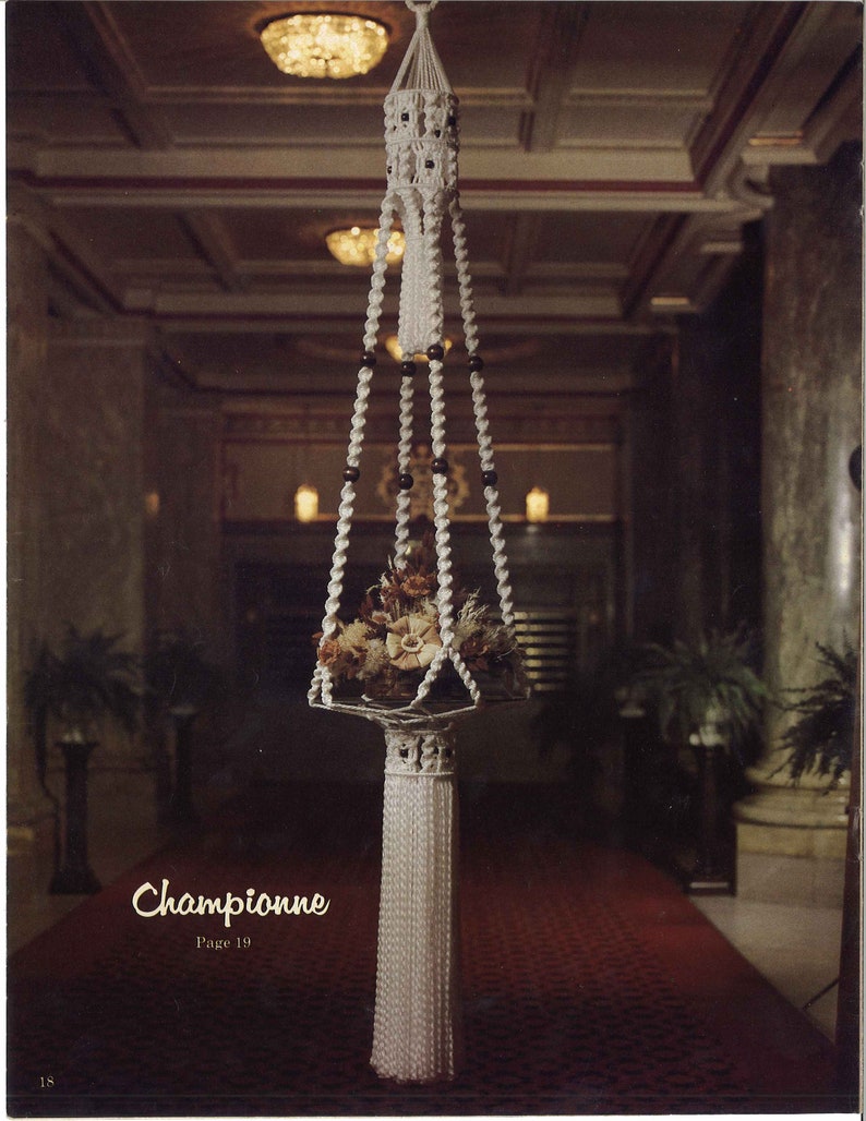 Peut inclure: Un porte-plante en macram&eacute; blanc avec un pompon, suspendu au plafond dans une pi&egrave;ce avec un tapis rouge. Le porte-plante est rempli de fleurs s&eacute;ch&eacute;es et comporte des perles noires sur les cordons.