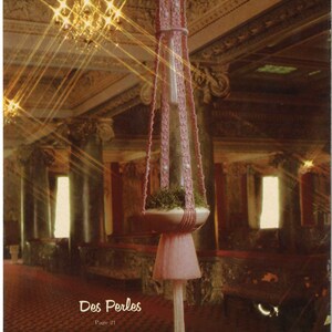 Peut inclure: Un porte-plante en macram&eacute; rose avec un pompon blanc suspendu au bas. Le porte-plante est dans une grande pi&egrave;ce orn&eacute;e avec un lustre.