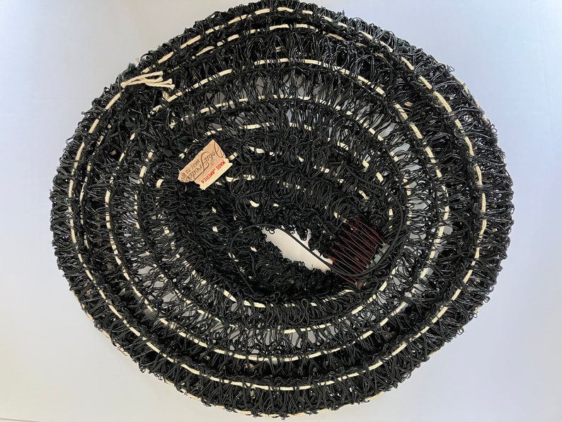 May include: A rolled-up black hair net with white accents and a brown comb. The net has a tag that reads "John Frederics Made in America". The hair accessory is circular and appears to be vintage.