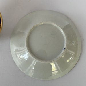 May include: White porcelain saucer with a blue rim and a small blue dot on the bottom.