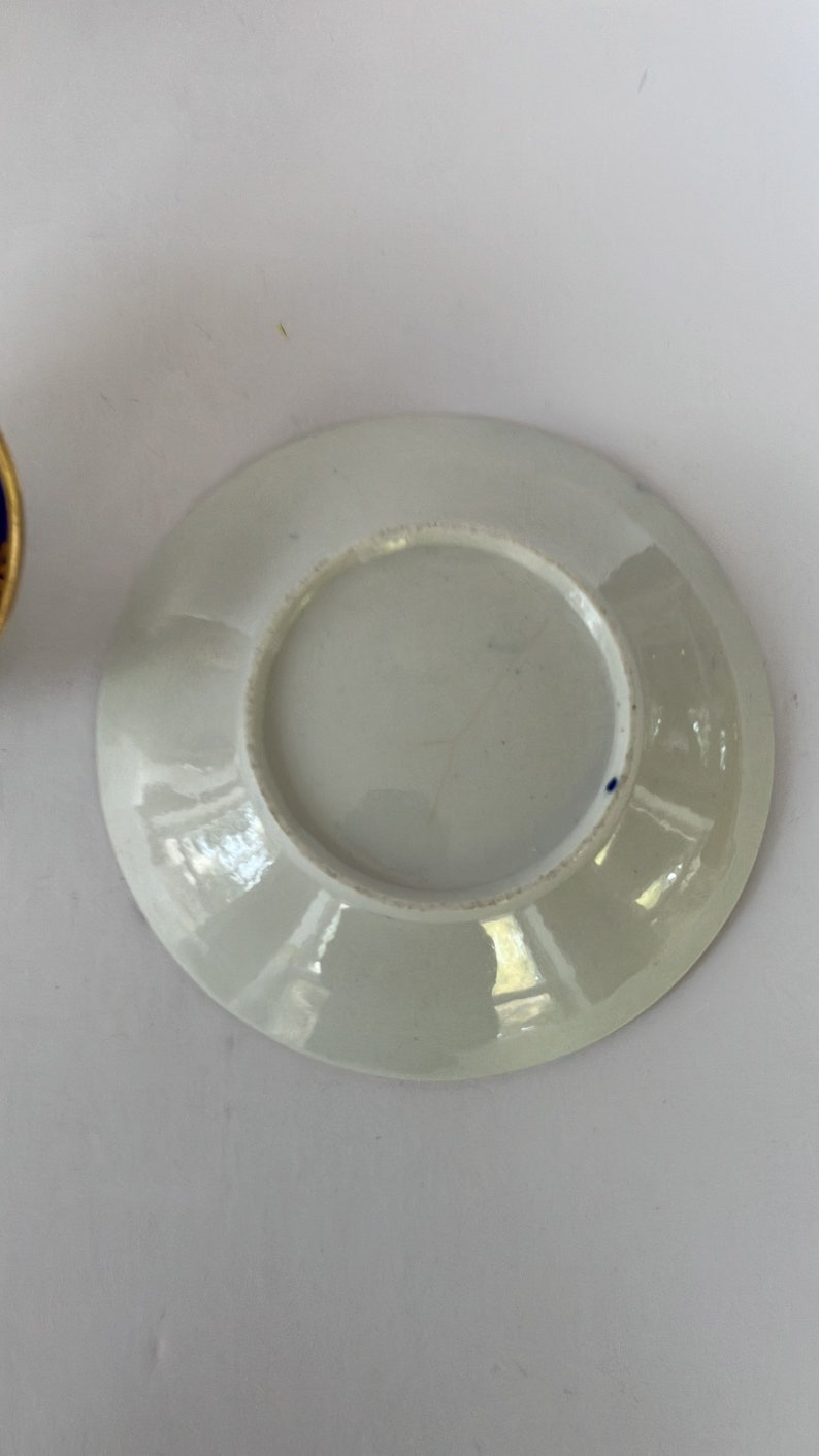 May include: White porcelain saucer with a blue rim and a small blue dot on the bottom.