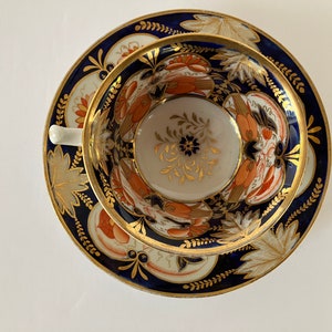 May include: A vintage teacup and saucer set with a blue and gold floral pattern. The cup and saucer are decorated with intricate details and a gold rim.