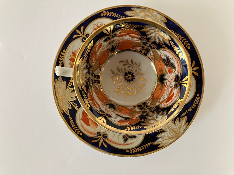 May include: A vintage teacup and saucer set with a blue and gold floral pattern. The cup and saucer are decorated with intricate details and a gold rim.