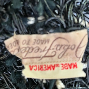 May include: Close-up of a vintage black hat with a woven design. A tag reads "John Frederics Made in America". The hat has a textured, open weave pattern, with a dark color scheme.