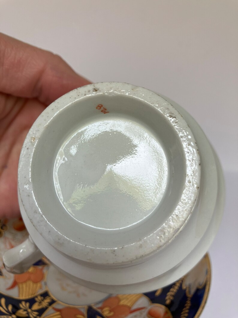 May include: The bottom of a white porcelain teacup with a brown number "128" printed on the bottom.