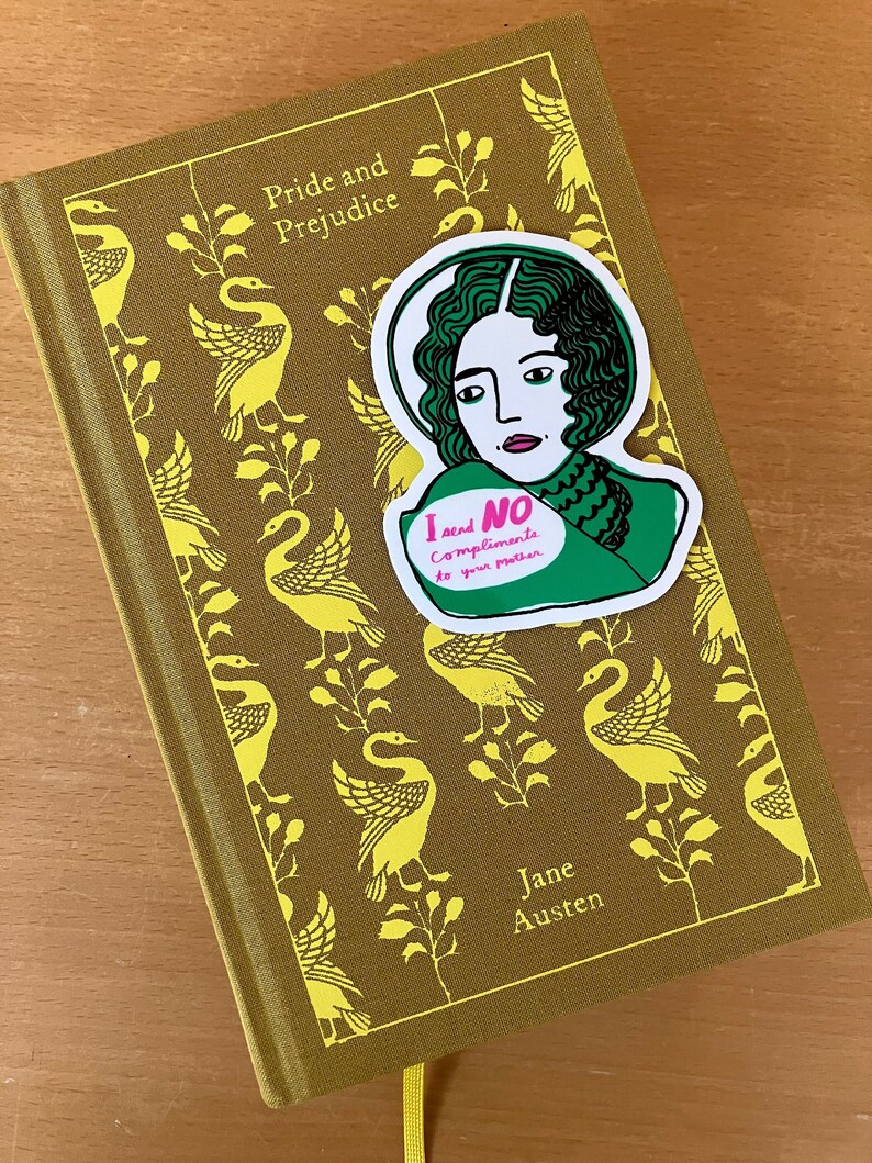 Puede incluir: Un libro de tapa dura de "Orgullo y Prejuicio" de Jane Austen, con una cubierta dorada con un patr&oacute;n de cisnes. Una pegatina con una ilustraci&oacute;n verde y blanca de una mujer y el texto "I send NO compliments to your mother" est&aacute; en el libro.