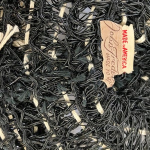 May include: Close-up of a woven textile with a complex pattern of black and off-white threads. The texture is dense and irregular, with a mix of looped and straight strands. A tag reads "John Freeda MADE TO ORDER MADE IN AMERICA."
