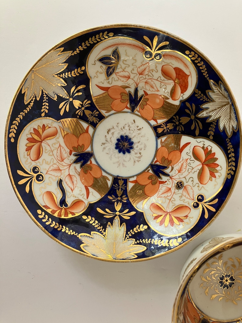 May include: A vintage porcelain teacup and saucer with a blue and white floral pattern. The saucer has a gold rim and intricate details. The teacup has a floral design in the center.