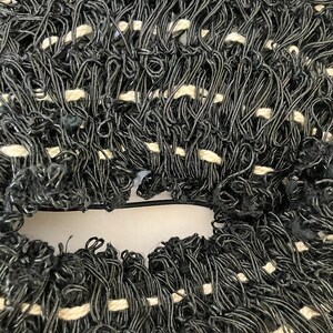 May include: Close-up of a woven textile with a dense, looped texture. The material is primarily black with interspersed white sections, creating a textured pattern. The weave appears to be made of a flexible, possibly synthetic, material.