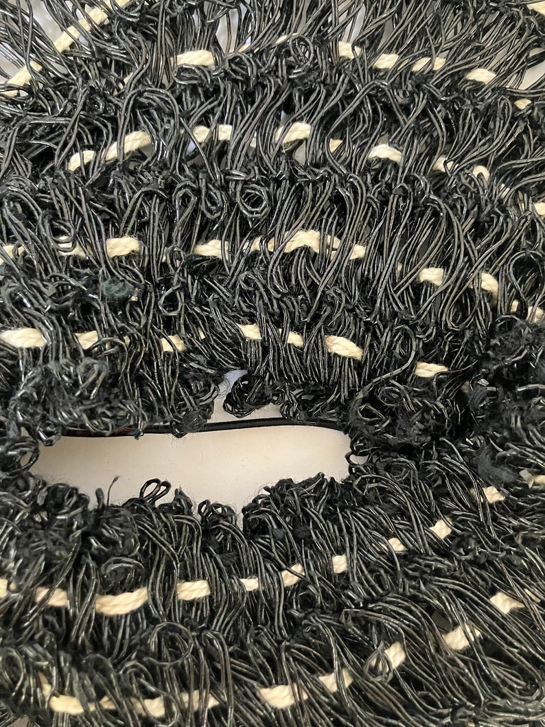 May include: Close-up of a woven textile with a dense, looped texture. The material is primarily black with interspersed white sections, creating a textured pattern. The weave appears to be made of a flexible, possibly synthetic, material.