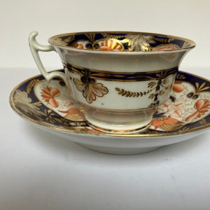May include: A vintage teacup and saucer set with a blue and gold floral pattern. The cup has a delicate handle and a wide, shallow bowl. The saucer has a matching design and a scalloped edge.