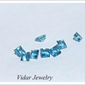 May include: A collection of light blue square-shaped gemstones on a white surface. The text "Vidar Jewelry" is printed below the gemstones.