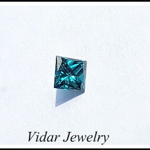 May include: A square-shaped, dark blue gemstone with a faceted cut. The gemstone is set against a white background.