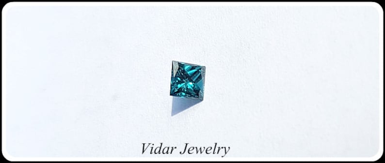May include: A square-shaped, dark blue gemstone with a faceted cut. The gemstone is set against a white background.