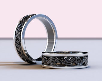 May include: Two silver wedding bands with black filigree designs. The bands are stacked on top of each other.
