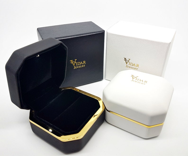 May include: Black and white jewelry boxes with gold accents. One box is open, revealing a black velvet interior. The boxes are branded with "VIDAR JEWELRY" in gold lettering. The boxes are octagonal and square shaped.