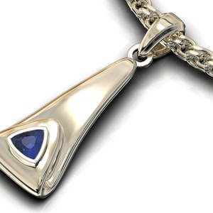 Puede incluir: Un collar de oro con un colgante triangular de piedra preciosa azul engastado en un marco de oro. El colgante está unido a una cadena de oro.