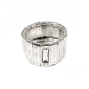 May include: A silver-toned stretch bracelet with a rectangular, textured design. The bracelet features a central rectangular clear stone. The metal has a distressed, vintage appearance, and the bracelet is set against a white background.