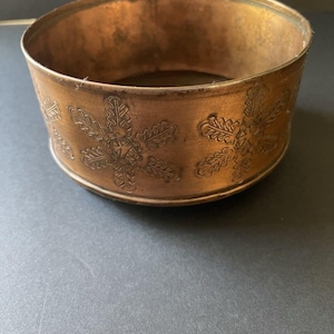 May include: A round, copper-colored metal planter with a snowflake design embossed around the rim.