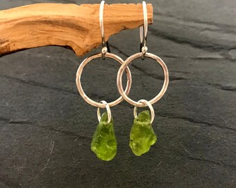 Puede incluir: Pendientes de aro de plata con gotas de piedras preciosas verdes. Los aros son martillados y tienen un acabado texturizado.