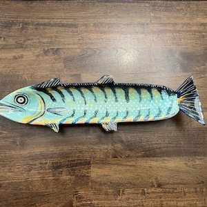 May include: A decorative, hand-painted fish-shaped serving platter. The platter is primarily turquoise with black, yellow, and blue accents. The fish has a detailed design with stripes and spots, and is placed on a wooden surface.