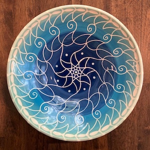 May include: A large, round ceramic bowl with a blue and white swirl design. The bowl is glazed in shades of blue, with a white swirl pattern that creates a spiral effect. The bowl is perfect for serving salads, pasta, or other dishes.