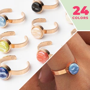 May include: A set of gold rings with colorful round stones. The stones have a marbled pattern. The rings are available in 24 colors.