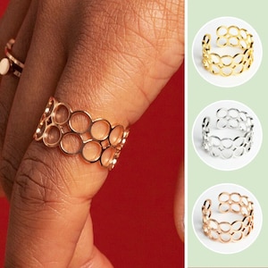 Könnte beinhalten: Ein goldener Ring mit einem mehrschichtigen Design aus ineinandergreifenden Kreisen. Der Ring wird an einem Finger getragen.