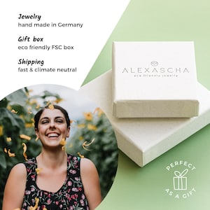 May include: A white gift box with the text "ALEXASCHA eco friendly jewelry" on the top. The box is sitting on a green surface. The text "PERFECT AS A GIFT" is printed on the bottom of the box.