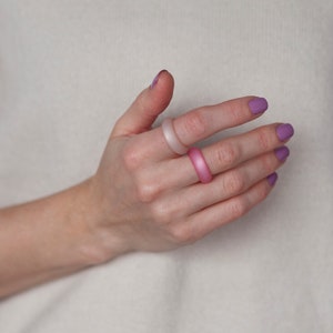 May include: A hand wearing three silicone rings. The rings are in shades of pink and purple.