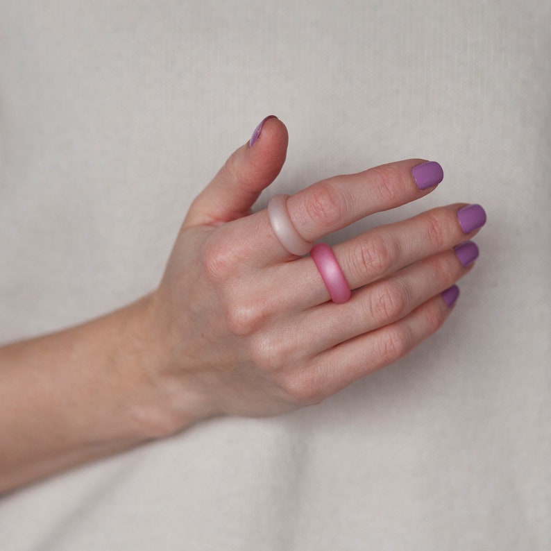 May include: A hand wearing three silicone rings. The rings are in shades of pink and purple.