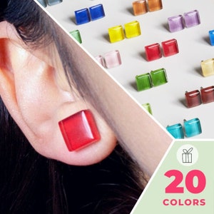 May include: A close-up of a person's ear wearing a pair of red square-shaped earrings. The image shows a variety of colourful square-shaped earrings in the background. The text "20 COLORS" is displayed in the bottom right corner of the image.