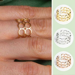 Könnte beinhalten: Ein Ring aus Gold, Silber und Roségold mit einem Doppelkreis-Design. Der Ring wird an einem Finger getragen.