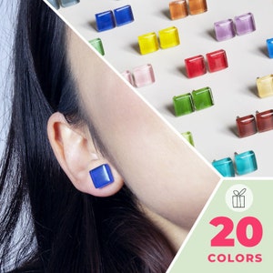 Peut inclure: Une femme portant une boucle d'oreille carrée bleue. L'image montre une variété de boucles d'oreilles carrées colorées dans différentes couleurs, notamment le rouge, le bleu, le vert, le jaune et le violet. Le texte "20 COULEURS" est affiché en bas de l'image.