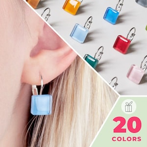 Könnte beinhalten: Quadratische Glas-Ohrhänger mit silberfarbenen Klappbügeln, erhältlich in 20 Farben, darunter Blau, Rot, Rosa und Bernstein. Die Ohrringe haben eine glatte, polierte Oberfläche und werden sowohl an einem Ohr als auch in einer Anordnung gezeigt.