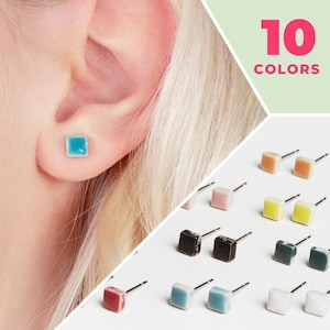Op de afbeelding: Tien kleuren vierkante keramische oorbellen. De oorbellen zijn klein en hebben een zilveren pin. De oorbellen worden getoond op een witte achtergrond.
