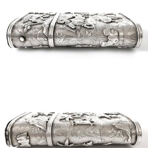 May include: A silver rectangular box with intricate embossed designs of flowers, leaves, and animals. The box has a hinged lid and a smooth, polished surface.