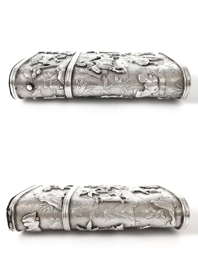 May include: A silver rectangular box with intricate embossed designs of flowers, leaves, and animals. The box has a hinged lid and a smooth, polished surface.