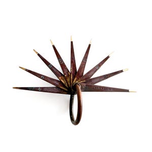 May include: A vintage brown metal gauge with multiple radiating blades, each marked with a number and tipped with gold. The blades are connected by a ring, and the gauge is set against a white background.