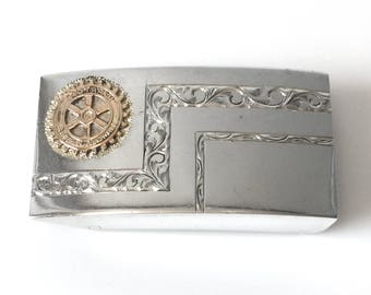 May include: Silver belt buckle with an engraved design and a gold Rotary International logo.