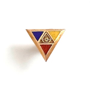 May include: A gold-toned triangular pin with a geometric design. The pin features a central emblem and three colored sections: blue, yellow, and red. The pin is set against a white background.