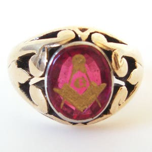 May include: A gold ring with a red stone featuring a gold Masonic symbol.